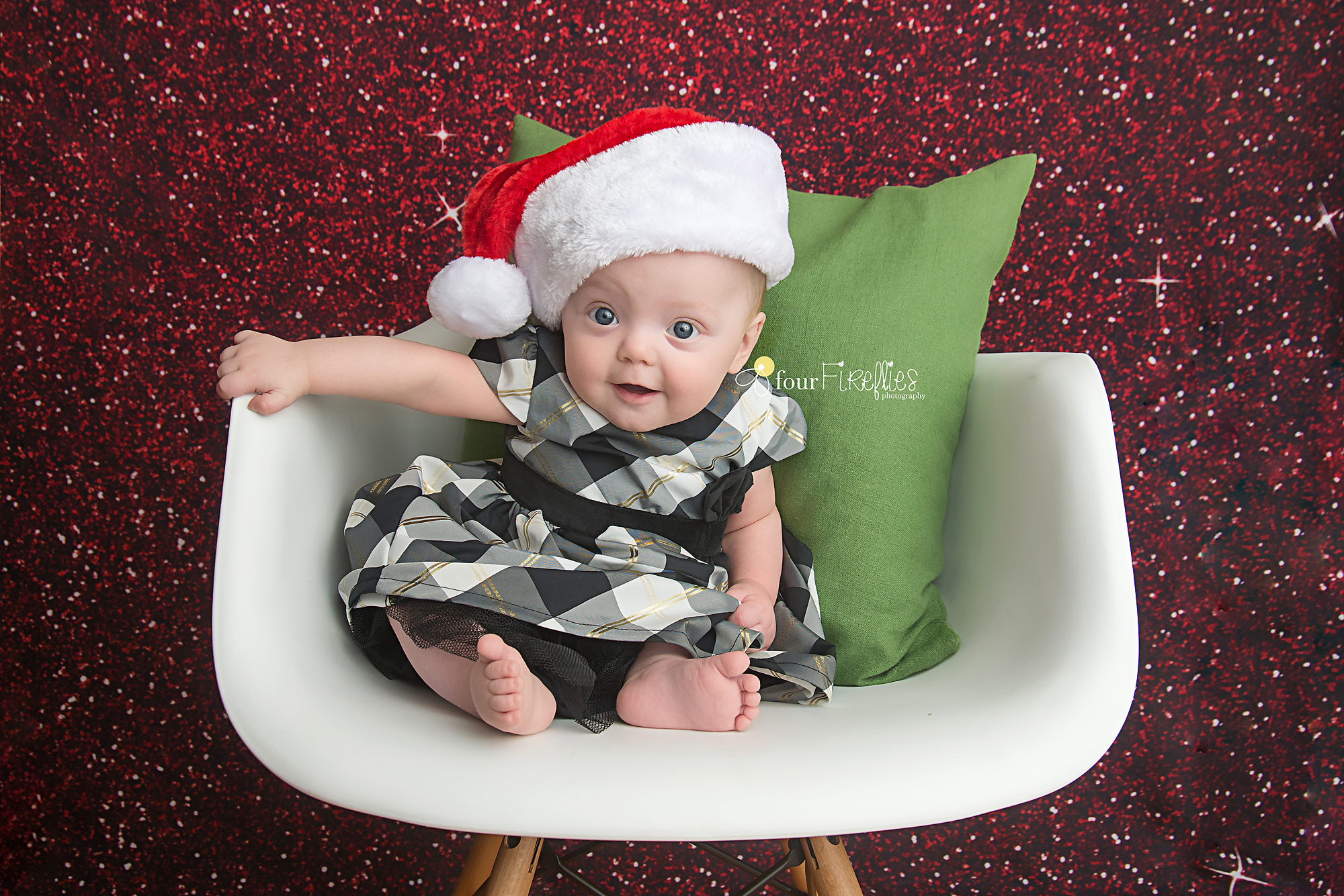 st-louis-baby-photographer-christmas-baby-in-plaid-dress-and-santa-hat-on-white-chair-with-green-pillow-and-red-glitter-backdrop.jpg