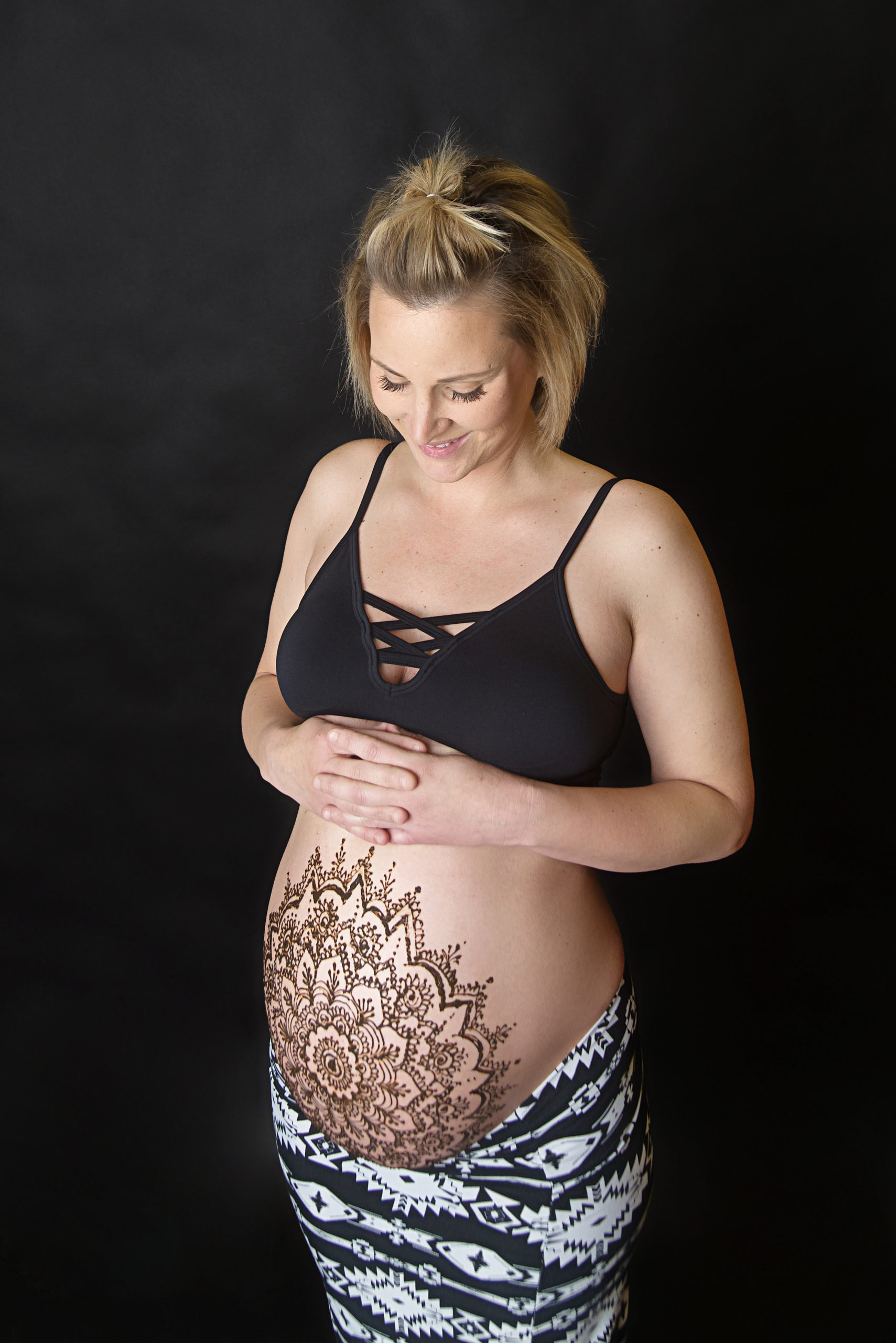 st-louis-maternity-henna-photography-mom-with-henna-on-pregnant-belly-on-black-background-looking-down.jpg