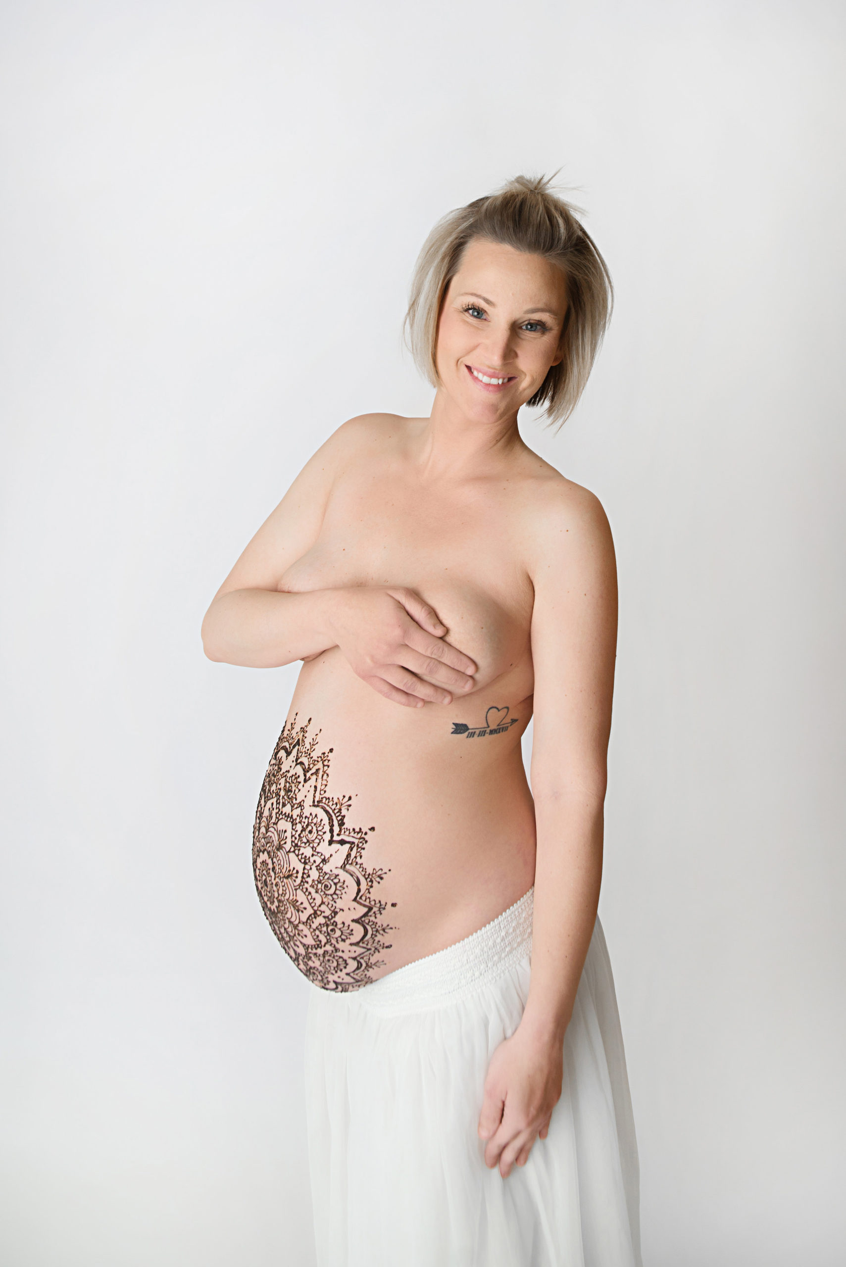 st-louis-maternity-henna-photography-pregnant-mom-on-white-backdrop-looking-at-camera-covering-breasts.jpg
