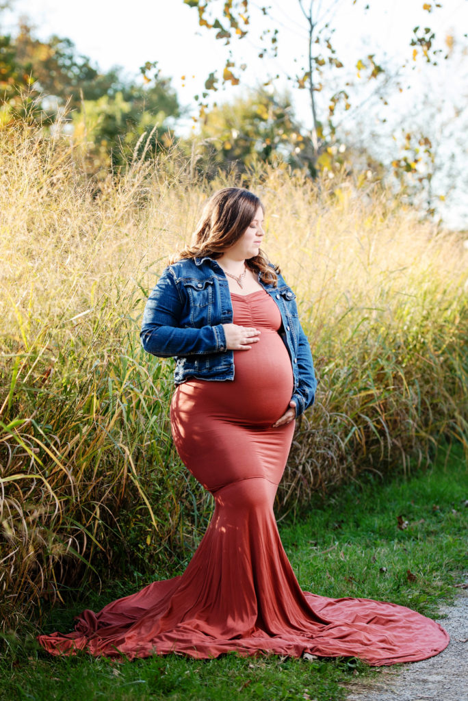 st-louis-fall-materntiy-session-pregnant-mom-in-rust-color-gown-and-jean-jacket-standing-in-tall-grass