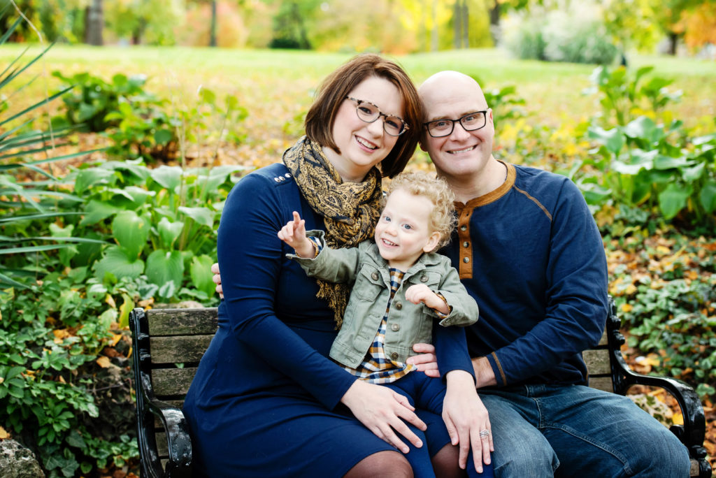 St-Louis-Fall-Mini-Sessions-mom-dad-and-and-daugher-sitting-on-bench-at-lafeyette-park-with-fall-colors
