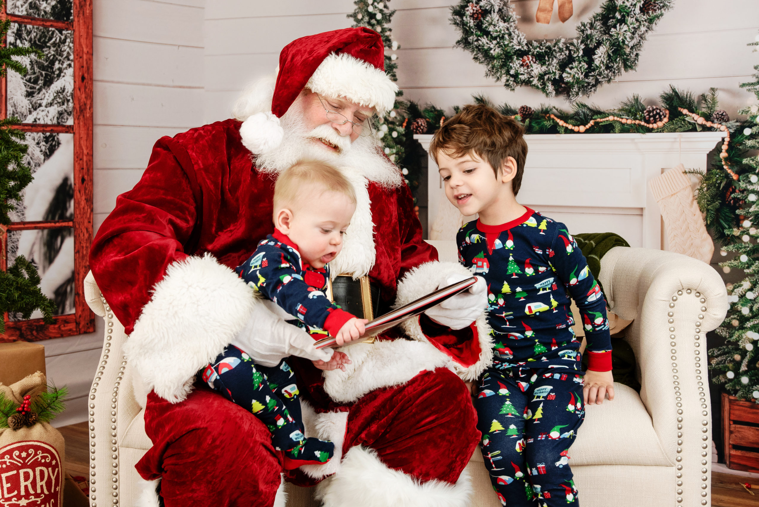 st-louis-santa-experience-santa-sitting-on-couch-with-two-boys-in-pajamas-opening-a-present