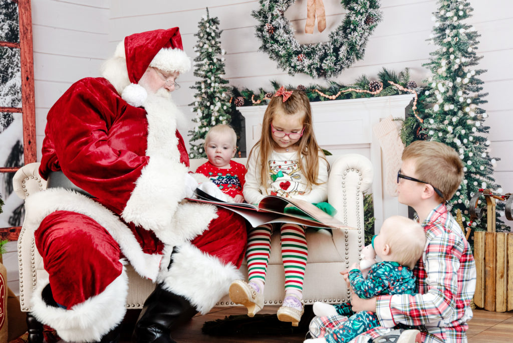 st-louis-santa-experience-santa-sitting-on-couch-with-a-group-of-kids-reading-a-book