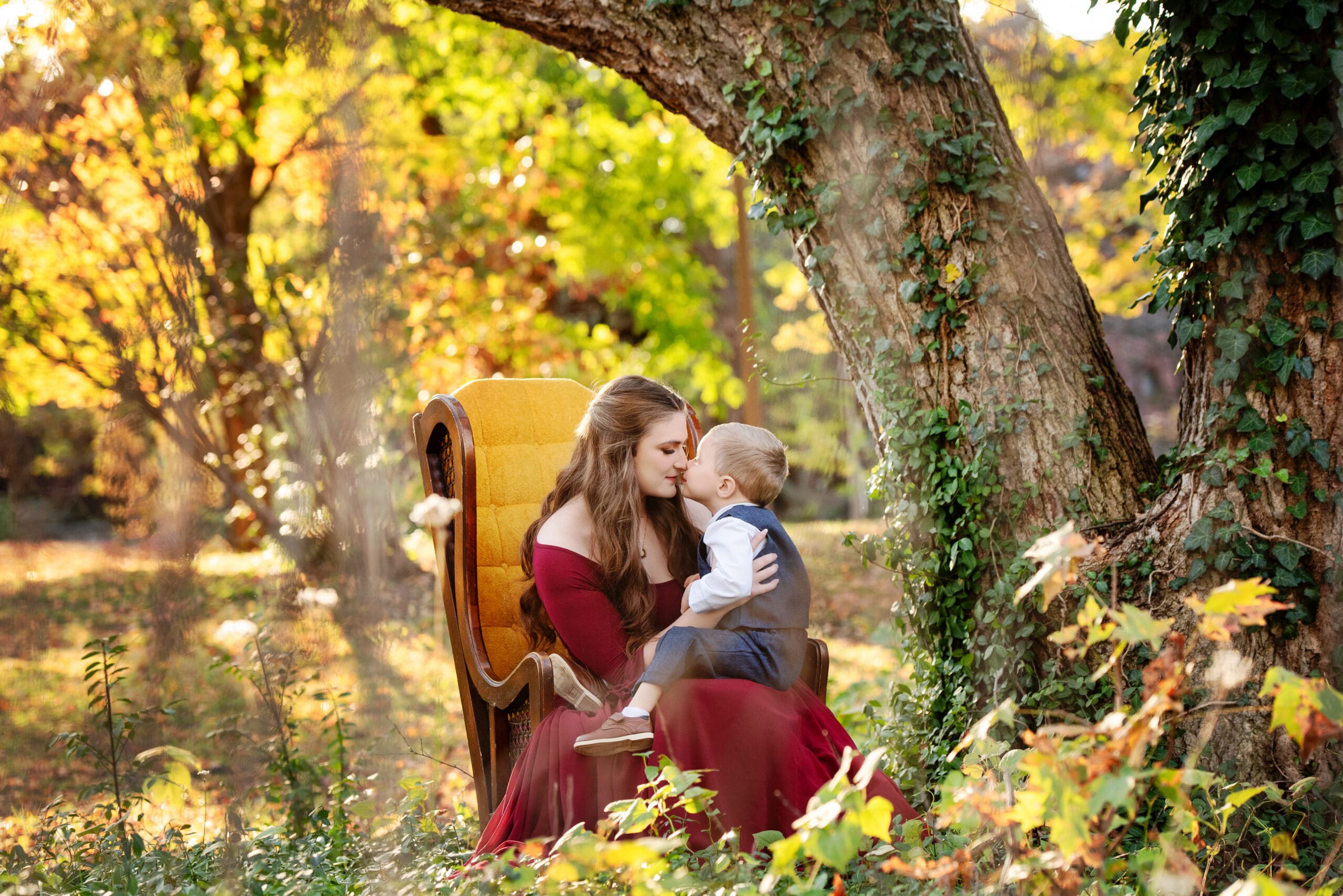 st-louis-fall-family-photographer-mom-and-son-touching-noses-while-sitting-in-chair-under-fall-tree