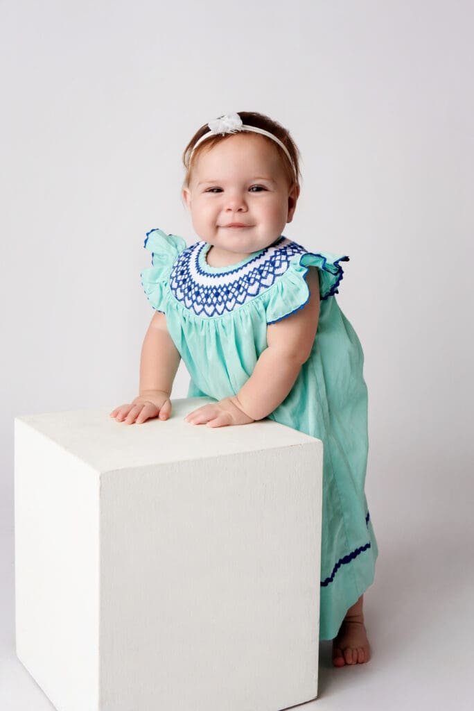 St. Louis Newborn Photographer standing milestone as part of first year minis. baby girl using block to stand wearing teal dress