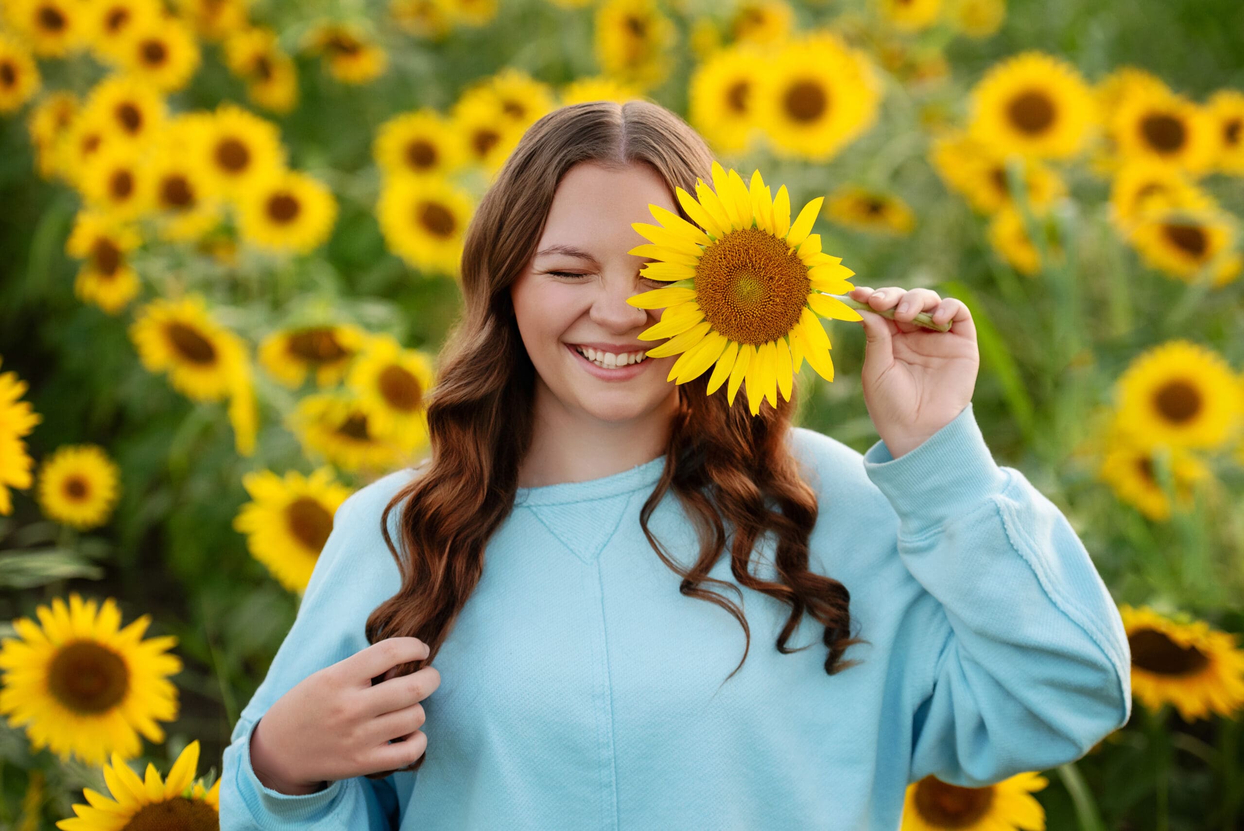 St-Lois-Senior-photographer-teen-girl-in-sunflower-feild-holding-sunflower-over-eye-and-smiling